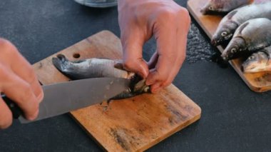 Adam ahşap tahta üzerinde balık sazan yüzgeçleri keser. Balık pişirme. Eller yakın çekim.