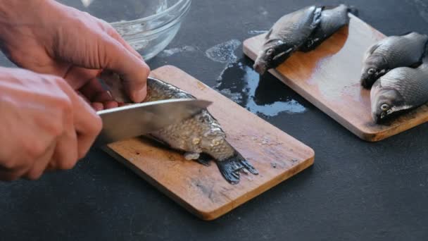 El hombre limpia la carpa de las escamas en el tablero de madera. De cerca las manos. Cocinar un pescado . — Vídeo de stock