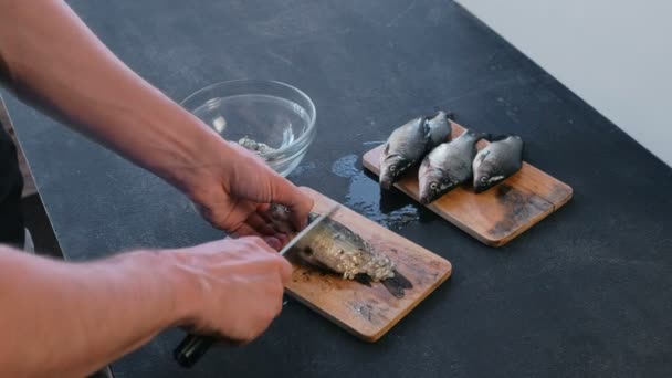 Mann reinigt Karpfen von der Schuppe auf Holzbrett. Hände aus nächster Nähe. Kochen einen Fisch. — Stockvideo