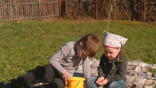 Bratr a sestra žížaly pohled sedí na trávníku v zahradě domu. — Stock video