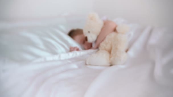 Seven-year-old boy wakes up hugging toy bear. Blur. — Stock Video