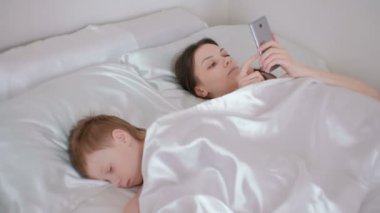 Annem uyandı ve cep telefonu internet tarama. Oğlunun hâlâ uyuyor..