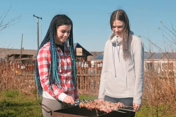 Dos amigas cocinan carne shashlik encima de la parrilla de carbón en el patio trasero. Hablando y sonriendo juntos . — Foto de Stock