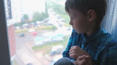 Çocuk yağmurda pencereden dışarı bakar ve üzücü.