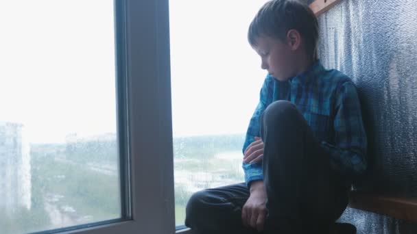 Boy looks out the window in the rain and is sad. — Stock Video