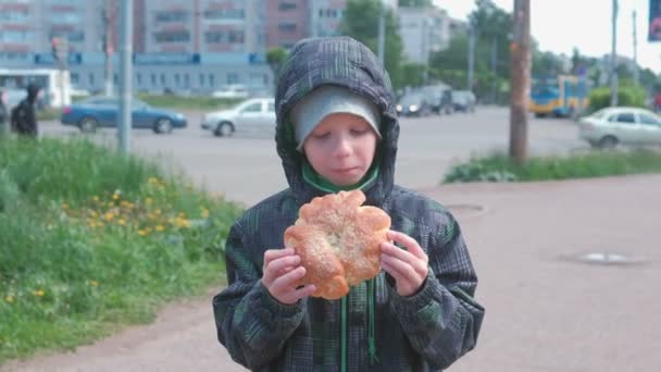 Мальчик ест булочку на улице . — стоковое видео