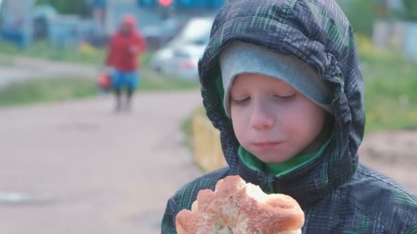 Хлопчик їсть булочку на вулиці . — стокове відео