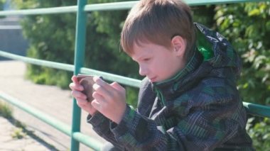 Çocuk parkta otururken cep telefonundan bir oyun oynuyor.