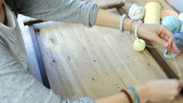 Плетение на ткацкой раме. Крупным планом женская рука кладет нитку в раму для ткачества. Вид сверху . — стоковое видео