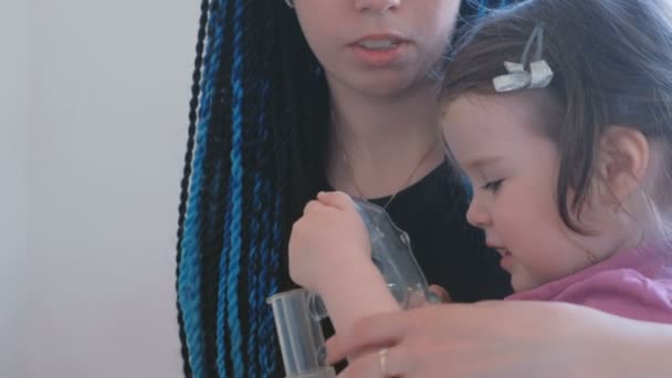 Kleines süßes Mädchen, das mit seiner Mutter durch die Atemmaske inhaliert. Vernebler und Inhalator für die Behandlung verwenden. — Stockvideo