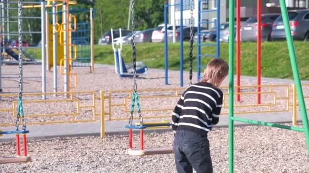 Επτά-έτος-παλαιό αγόρι κουνιέστε σε μία κούνια, στην παιδική χαρά. — Αρχείο Βίντεο
