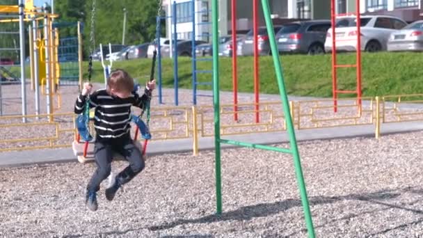 Sedm rok starý chlapec houpat na houpačce na hřišti. — Stock video