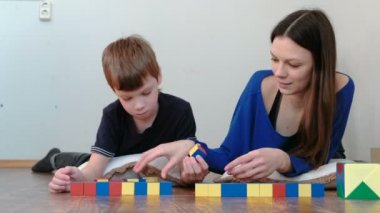 Anne ve oğlu yerde yatarken ahşap renkli eğitim oyuncak blokları ile birlikte oynuyor. Oğlu tahta küpleri annesinden alır..