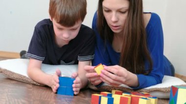 Anne ve oğlu birlikte ahşap renkli eğitim oynayan yerde yatarken blok oyuncak. Mavi bir kutu inşa.