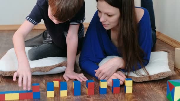 Einen Turm aus Blöcken und Würfeln zu bauen. Mutter und Sohn spielen zusammen mit auf dem Boden liegenden farbigen Holzspielzeugklötzen. — Stockvideo