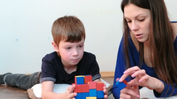 Einen Turm aus Blöcken und Würfeln zu bauen. Mutter und Sohn spielen zusammen mit auf dem Boden liegenden farbigen Holzspielzeugklötzen. — Stockvideo