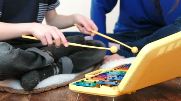 Playing music instrument. Closeup boys hands playing on xylophone with sticks and his mom sitting near him. — Stock Video