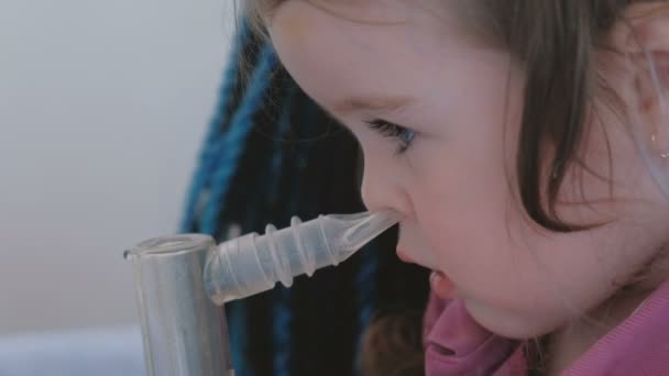 Маленькая милая девочка вдыхает через маску ингалятора со своей мамой. Использование ингалятора и распылителя для лечения . — стоковое видео