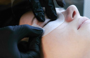 Güzellik bakımı. Güzellik uzmanları eller kadının gözlerinin altında yamalar yapıştırın. Yan görünüm.