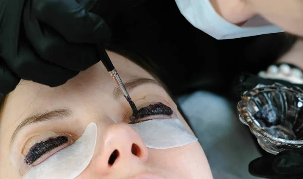 Tratamiento de belleza. El cosmetólogo pone pintura negra en las pestañas. Laminando pestañas. Ojos de cerca . — Foto de Stock