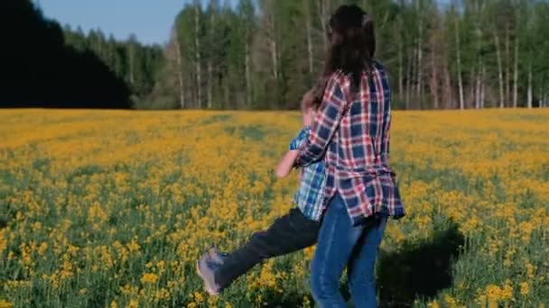 Mutter und Sohn drehen sich Händchen haltend auf dem Feld mit gelben Blumen. Familienwanderung im Frühling. — Stockvideo