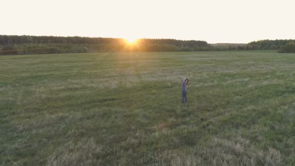 Oigenkännlig kvinna gå på fältet vid solnedgången armarna utsträckta. — Stockvideo