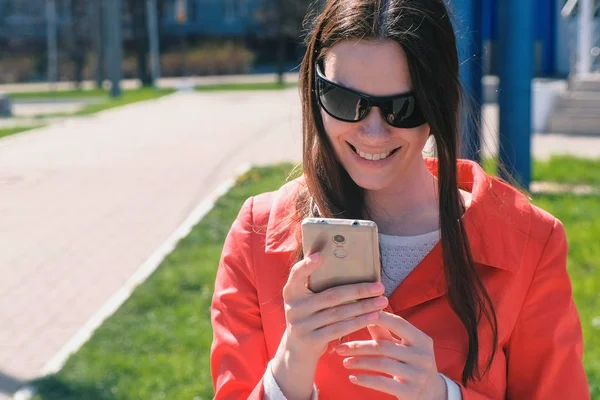 Retrato de mujer feliz en abrigo rojo espera a alguien y comprueba su teléfono, mensajes de texto . — Foto de Stock