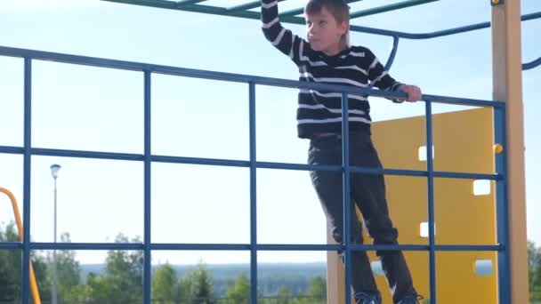 Niño sube en una pared de escalada sosteniendo la cuerda en el patio de recreo . — Vídeo de stock