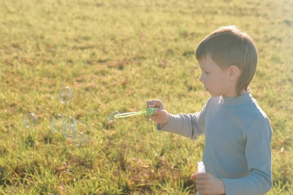 Мальчик делает мыльные пузыри на лугу и играет в теплый весенний день . — стоковое фото