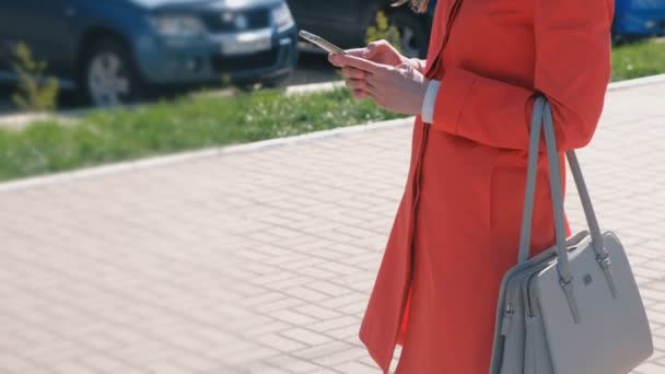 Oigenkännlig kvinna i röd kappa väntar på någon och kontrollerar hennes telefon, skicka SMS. Närbild händer. Sidovy. — Stockvideo