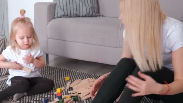 Маленька чарівна блондинка грає в дерев'яні блоки з мамою, що сидить біля дивана . — стокове відео