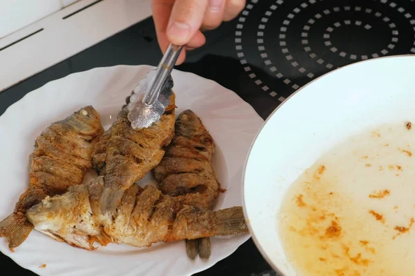 O homem põe o peixe de carpas em um prato da panela de ato de fritar. Mãos de homem close-up com pinças culinárias. — Fotografia de Stock