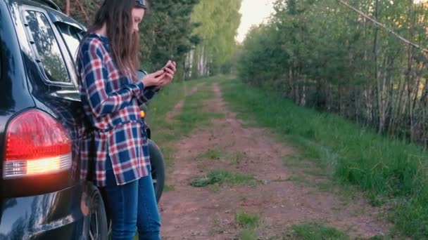 Vrouw doet een beroep op de telefoon en vraagt om hulp bij een gebroken auto. In een woede schopt het stuur van een auto. — Stockvideo