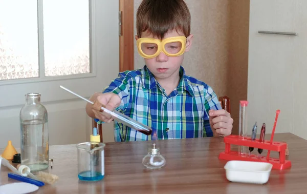 Experiências de química em casa. Menino aquece o tubo de teste com líquido vermelho na lâmpada de álcool em chamas . — Fotografia de Stock