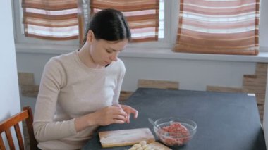 Kadın kıyma etli köfte yapar, kamera ve gülümsüyor görünüyor.