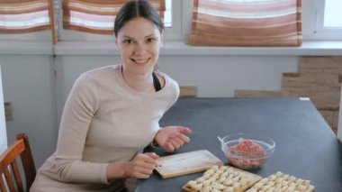 Kadın kıyma etli köfte yapar, kamera ve gülümsüyor görünüyor.