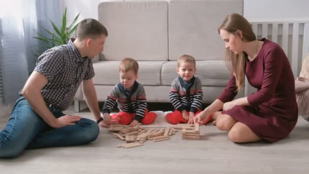 Οικογένεια μαμά, μπαμπάς και δύο δίδυμα αδέλφια παίζουν μαζί κτηρίου από ξύλινα μπλοκ στο πάτωμα. — Αρχείο Βίντεο