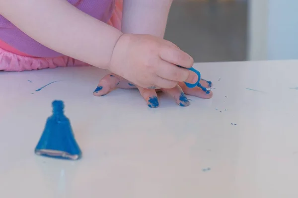 Piccola ragazza carina dipinge le unghie con vernice blu. Mani in primo piano . — Foto Stock
