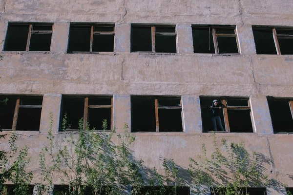 Женщина, стоящая на окне разрушенного многоэтажного здания со многими разбитыми окнами . — стоковое фото