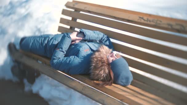 Junge Frau schläft im Winter im Park auf einer Bank. — Stockvideo
