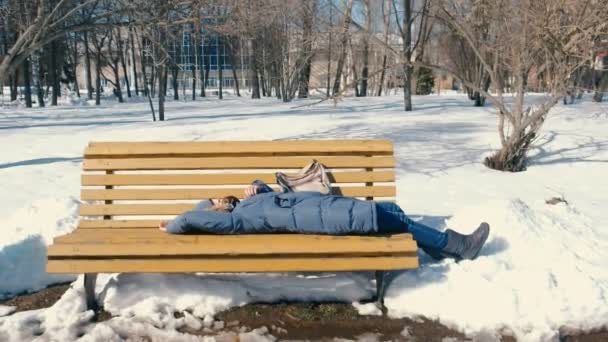 Mujer joven cansada duerme en el parque en un banco en el invierno . — Vídeo de stock