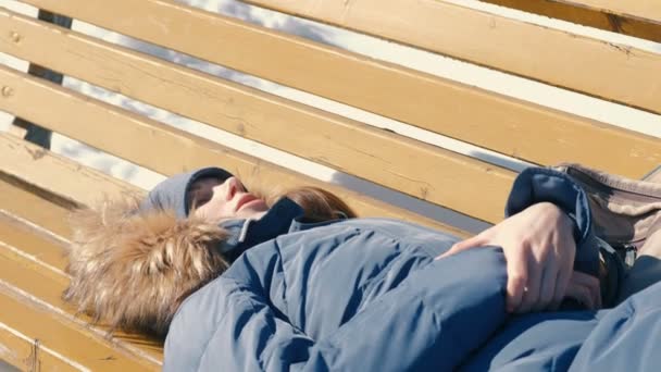 Mujer joven cansada duerme en el parque en un banco en el invierno . — Vídeo de stock