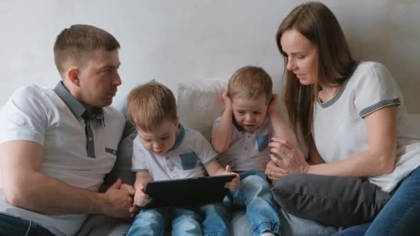 Famille avec tablette. Maman, papa et deux fils jumeaux tout-petits regardant dessin animé à la tablette couché sur le lit . — Video