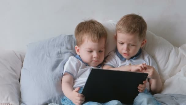 Niños con tableta. Dos niños gemelos niños pequeños mirando dibujos animados en la tableta acostado en la cama . — Vídeos de Stock