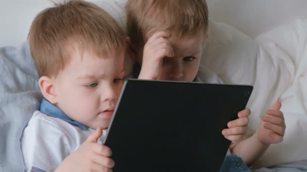 Дети с планшетом. Два мальчика близнецы малыши смотрят мультфильм на планшет, лежащий на кровати . — стоковое видео