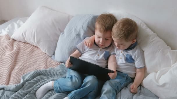 Дети с планшетом. Два мальчика близнецы малыши смотрят мультфильм на планшет, лежащий на кровати . — стоковое видео