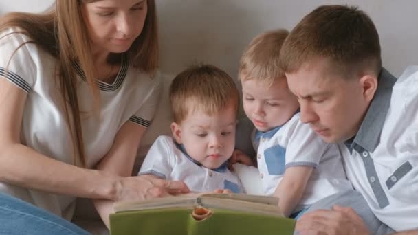 Mãe de família, pai e dois irmãos gêmeos lêem livros deitados na cama. Tempo de leitura da família . — Vídeo de Stock