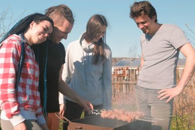 Grup Genç insanlar arkadaşlar Barbekü şaşlık et arka bahçesinde üzerinde kömür ızgara üzerine. Konuşmak ve birlikte gülümseyen.