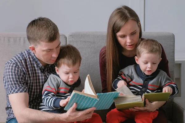 Famille maman, papa et deux frères jumeaux lisent des livres assis sur le canapé. Temps de lecture en famille . — Photo