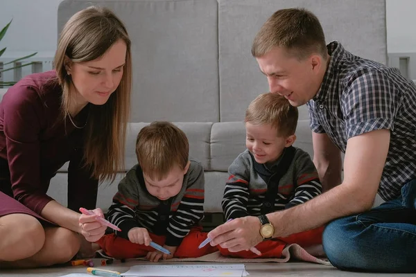 Rodzina Mama, Tata i dwóch braci bliźniaków zetknąć ze sobą markery i czuł długopisy, siedząc na podłodze. — Zdjęcie stockowe